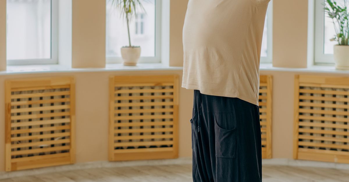 Elderly man performing a gentle standing stretch on a yoga mat