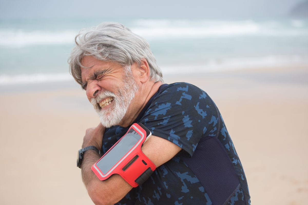Older man holding his shoulder in discomfort during a seaside walk